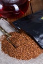 Infuser with dry rooibos leaves on grey wooden table, closeup
