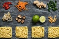 Ingredients for asian dish. Dried asian noodles with lime, nuts, cilantro and vegetables on wooden background