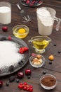 Ingredients for baking berry pie. Flour in black plate, cocoa powder. Measuring cup with flour, glass of milk, broken egg and salt