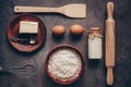 Ingredients for baking on a dark rustic background, flour, butter, eggs, rolling pin, whisk and paddle. Top view, flat lay