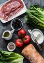 Ingredients for bruschetta - prosciutto, ciabatta bread, romano salad, olives, tomatoes, cream cheese on a dark background, top
