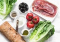 Ingredients for bruschetta - prosciutto, ciabatta bread, romano salad, olives, tomatoes, cream cheese on a light background, top