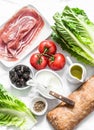 Ingredients for bruschetta - prosciutto, ciabatta bread, romano salad, olives, tomatoes, cream cheese on a light background, top