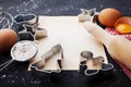 Ingredients for christmas baking. Cookies cutters, flour, rolling pin, eggs and paper sheet on kitchen black table. Royalty Free Stock Photo