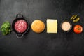 Ingredients for cooking burgers. Minced beef patties, buns, tomatoes, herbs and spices, on black stone background, top view flat Royalty Free Stock Photo
