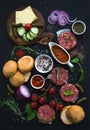 Ingredients for cooking burgers. Raw ground beef meat cutlets, buns, red onion, cherry tomatoes, greens, pickles, tomato Royalty Free Stock Photo