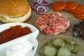 Ingredients for cooking burgers. Raw ground meat cutlets on wooden background, red onion, tomatoes, greens, pickles, tomato s
