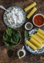 Ingredients for cooking fresh cannelloni pasta with spinach and ricotta baked with mozzarella cheese in a baking dish on a wooden