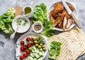 Ingredients for cooking greek gyros - chicken schnitzel, lettuce, tortillas, greek yogurt sauce, tomatoes, olives on a gray