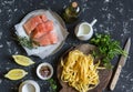 Ingredients for cooking lunch - raw salmon, dry pasta tagliatelle, cream, olive oil, spices and herbs. On a dark background Royalty Free Stock Photo