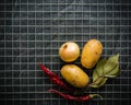 Ingredients for cooking: potatoes, salt, pepper, onion, garlic on a dark stone table. Metal grid. Royalty Free Stock Photo