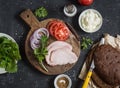 Ingredients for cooking sandwich - roasted pork, tomato, red onion, arugula, rye bread, soft cheese.