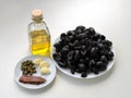 Ingredients for cooking tapenade: pitted black olives on white plate, olive oil in glass bottle, three cloves of garlic, some