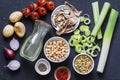 Ingredients for detox soup - bouillon in bottle, celery, chickpeas, leeks, tomatoes, red onions, spices on dark background, top vi