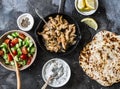 Ingredients for greek chicken gyros - fried chicken, tomato cucumber salad, tzatziki sauce and flatbread on a dark background, top