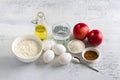 Ingredients for homemade apple pie: apples, flour, eggs, water, oil, sugar, cinnamon, salt on a light gray textured background