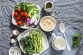 Ingredients for lunch - orzo pasta, asparagus, green peas, broccoli, cherry tomatoes, olive oil, cream and spices. On a gray backg