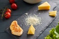 Ingredients for making salad. Piece and grated parmesan cheese on black serving board, cherry tomatoes