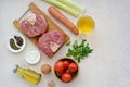 Ingredients for ossobuco, beef shank stew on a bone with carrots, tomatoes and celery on a light concrete background. Main meat Royalty Free Stock Photo