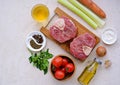 Ingredients for ossobuco, beef shank stew on a bone with carrots, tomatoes and celery on a light concrete background. Main meat Royalty Free Stock Photo