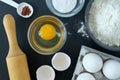 Flour, baking powder, cinnamon, eggs and rolling pin for rolling dough on a black background