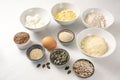 Ingredients for a protein bread with quark, oat bran, lupine flour, almond and various seeds in bowls on a white table, healthy