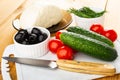 Ingredients for salad. Cheese in saucer, bowls with dill, black olives, cucumbers, tomato cherry, knife on cutting board on wooden Royalty Free Stock Photo