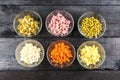 Ingredients shredded for salad in transparent plates on a black wooden background. Olives, pickled cucumbers, sausages, carrots, p Royalty Free Stock Photo