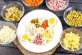 Ingredients shredded for salad in transparent plates on a black wooden background. Olives, pickled cucumbers, sausages, carrots, p Royalty Free Stock Photo