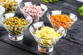 Ingredients shredded for salad in transparent plates on a black wooden background. Olives, pickled cucumbers, sausages, carrots, p Royalty Free Stock Photo