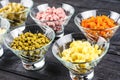 Ingredients shredded for salad in transparent plates on a black wooden background. Olives, pickled cucumbers, sausages, carrots, p Royalty Free Stock Photo