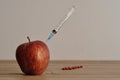 An injection needle stuck into an apple with red pills