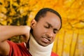 Injured black hispanic male wearing neck brace, holding hands in pain around support making faces of agony, yellow Royalty Free Stock Photo