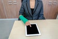 Injured businesswoman with broken hand and green cast on the wrist using tablet computer in office
