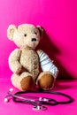 Injured teddy bear with a bandage and stethoscope, pink background