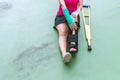 Injured woman wearing sportswear painful arm with gauze bandage, arm cast and wooden crutches sitting on floor