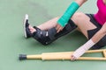Injured woman wearing sportswear painful arm with gauze bandage, arm cast and wooden crutches sitting on floor