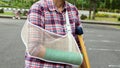 injury woman with broken arm wearing an arm sling and green cast