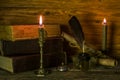 The inkwell with a feather, old documents and books, burning candles stand on a wooden table Royalty Free Stock Photo