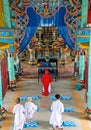 Inner hall of Cao Dai Church (Caodaism) with praying priest and believers in white robes, colorful altar