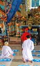 Inner hall of Cao Dai Church (Caodaism) with praying priest and believers in white robes, colorful altar