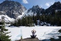 Inner peace and mindfulness. Woman meditating on scenic lake shore with beautiful view of snow covered mountains.