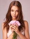 Innocence and beauty. Beautiful young woman holding a bunch of pink flowers against a pink background. Royalty Free Stock Photo