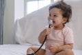 Innocence toddler girl sitting on the white bed while holding stethoscope in her hand at home. Mixed race little doctor baby Royalty Free Stock Photo