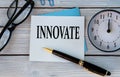 INNOVATE - word on a white sheet on a light wooden background with an alarm clock
