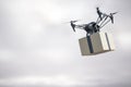 Innovative fast delivery service with modern grey quadrocopter carrying cardboard box in the air at gloomy background.