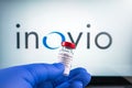 Inovio logo and covid-19 coronavaccine injection vial held with blue medical gloves.