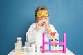 Inquisitive child girl looking at a test tube through a magnifying glass on blue background