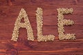 The inscription of ale by malt grains on wood background. Craft