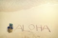 Inscription Aloha written on the sandy beach with ocean wave